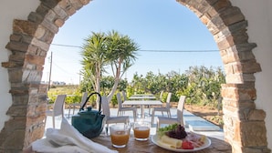 An outdoor dining area with a stone archway, a table set with plates of food, glasses, and a teapot. - Ktima Bianco (Naxos)
