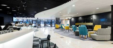 A modern lobby with a curved reception desk, seating area with various chairs, and a large window providing a view of the city.