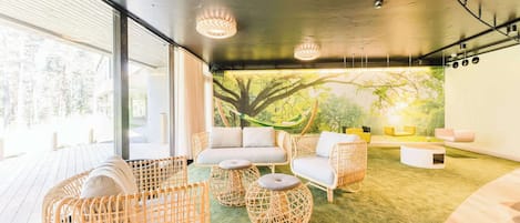 A modern interior with wicker furniture, a green carpet, and a large window with a view of trees.