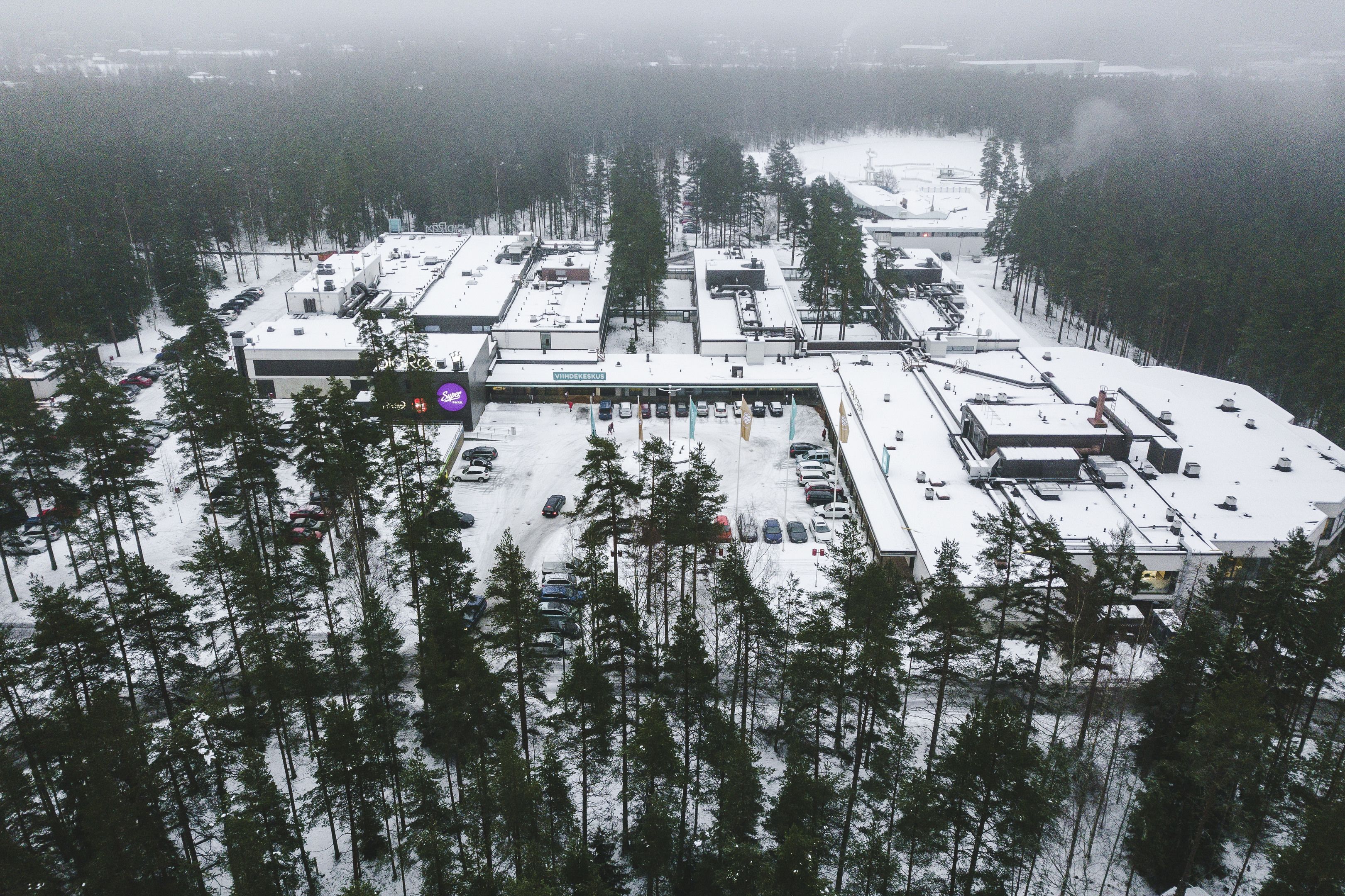 Vista aérea de un estacionamiento cubierto de nieve, con varios edificios y automóviles estacionados.