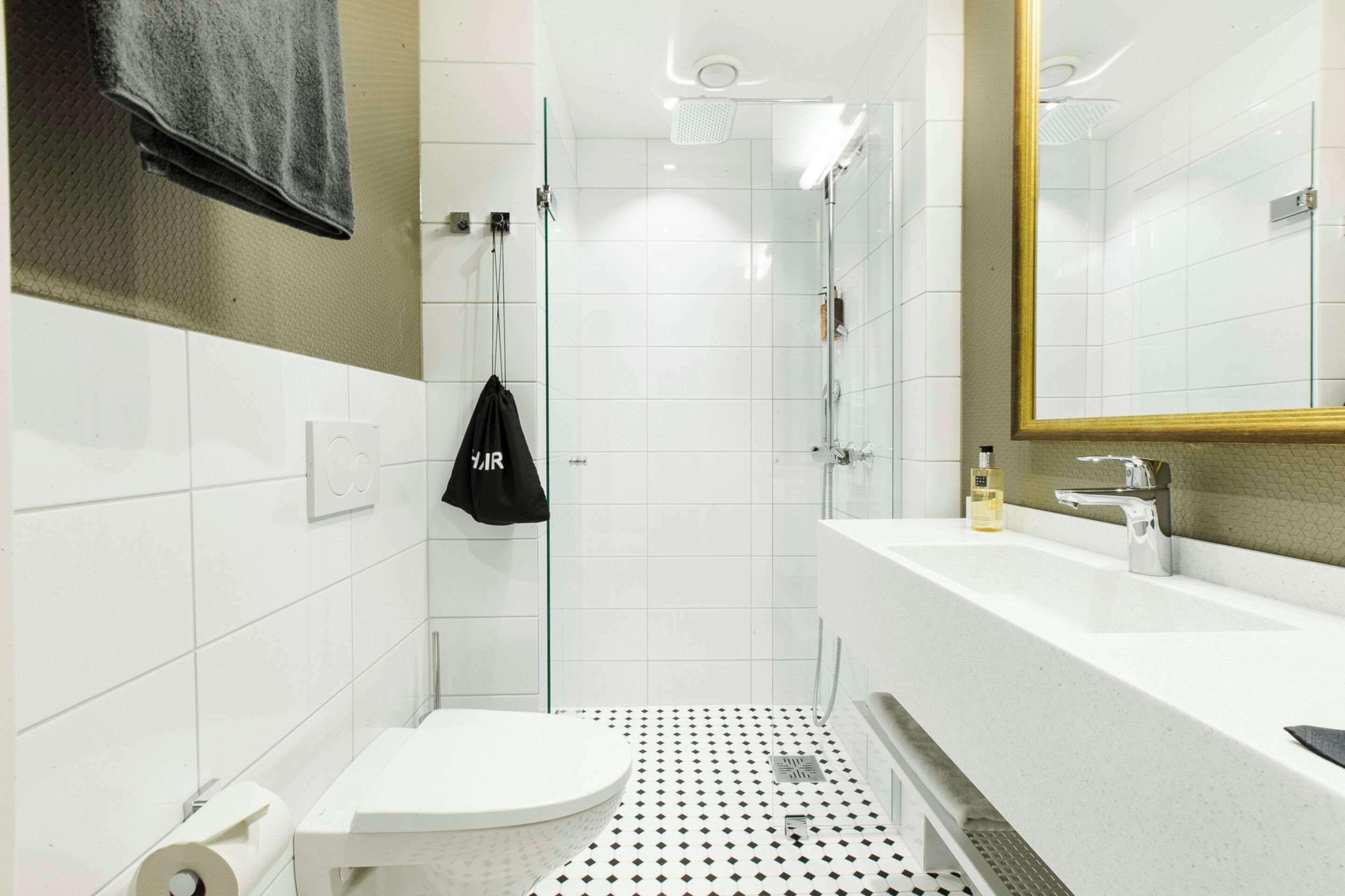 Un baño moderno con inodoro blanco, cabina de ducha de vidrio y lavamanos blanco con espejo de marco dorado.