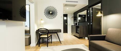 A modern living room with a flat-screen TV, a dining area with a chair, a sofa, and a coffee table with magazines.
