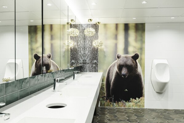 A modern bathroom with a bear mural, a large mirror, and a urinal. - Quality Hotel Sveitsi (Hyvinkaa)