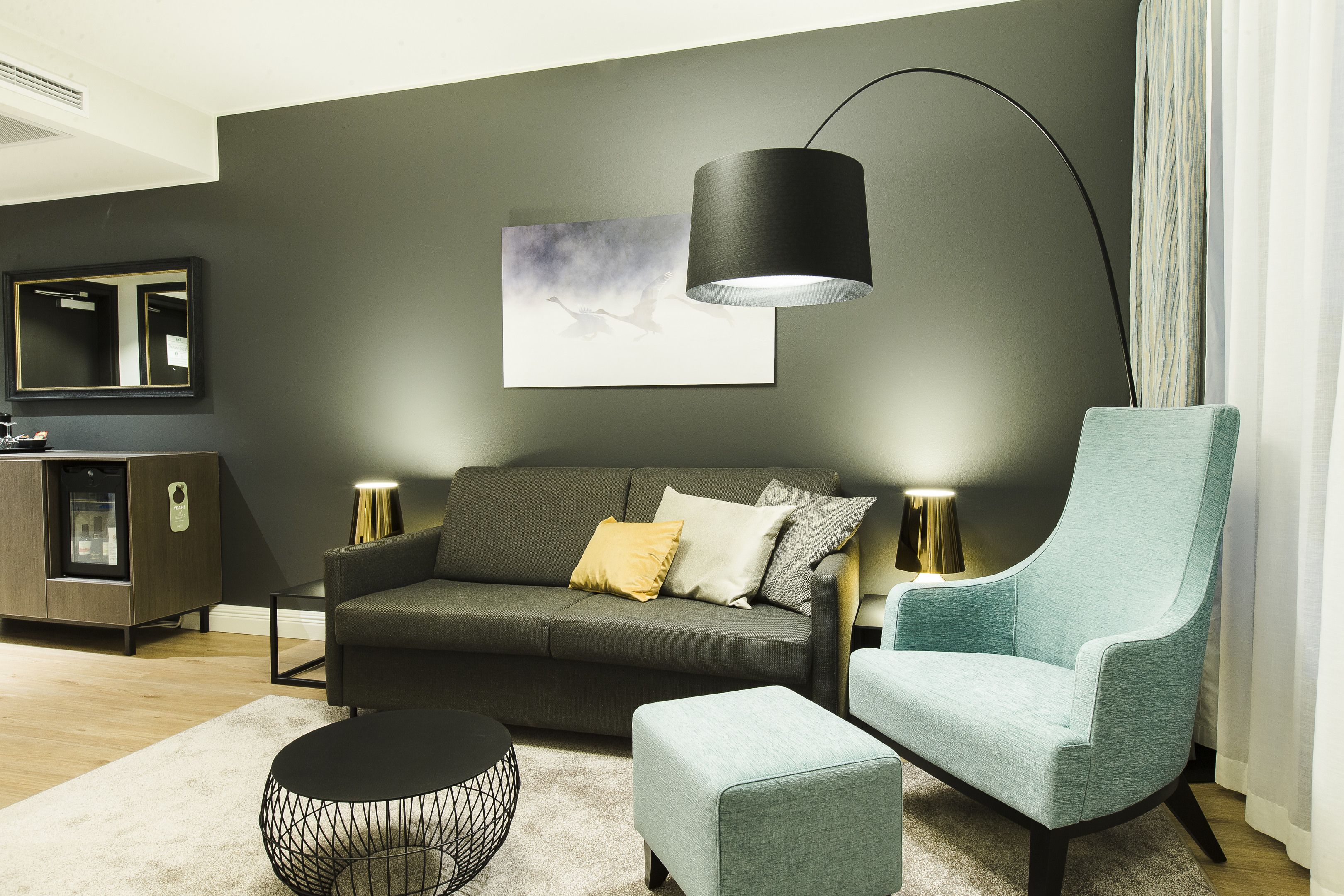 Una sala de estar moderna con un sofá gris oscuro, un sillón azul claro, una mesa redonda de centro y una lámpara de pie.