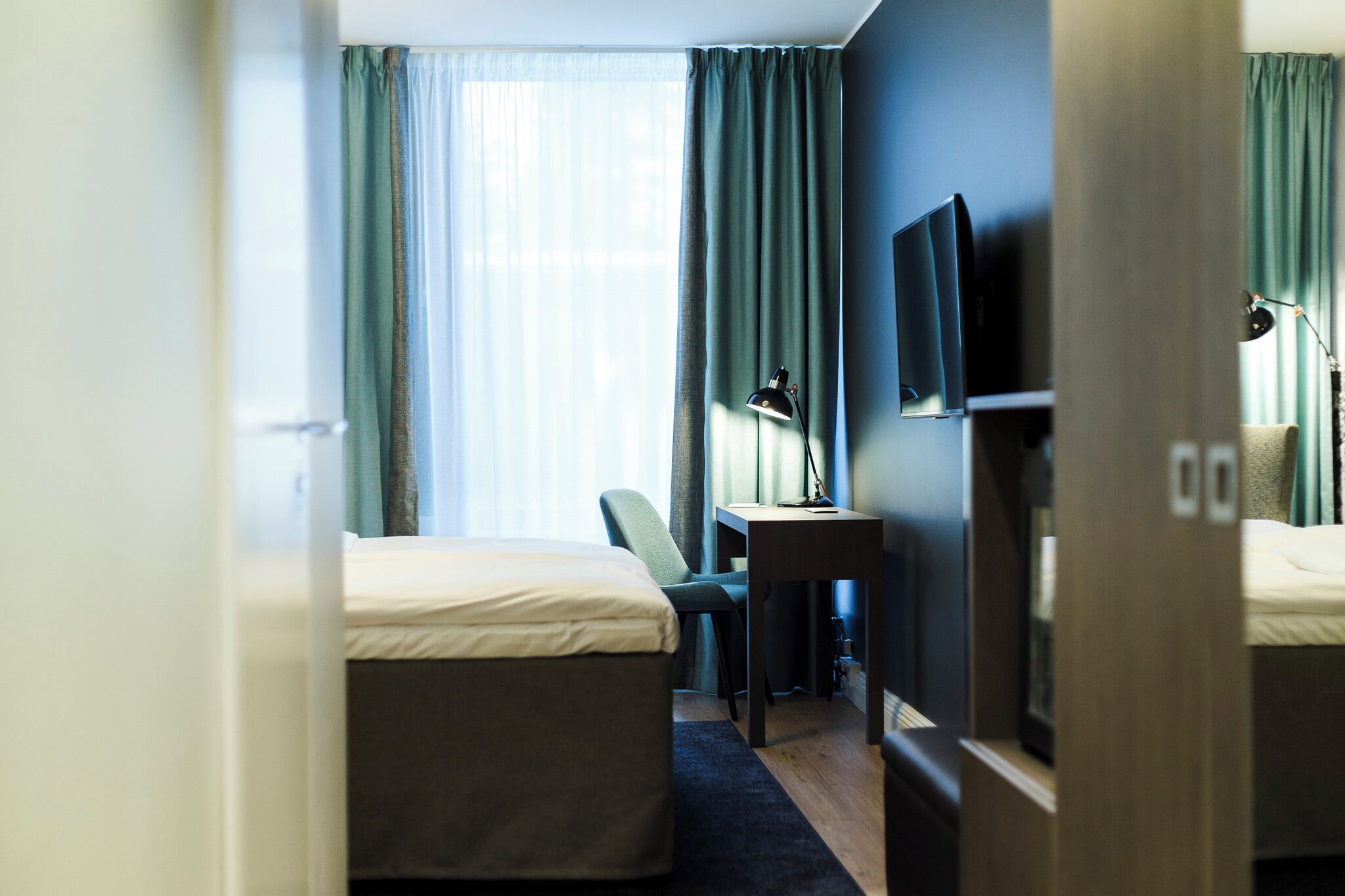 A hotel room with a bed, desk, chair, TV, and curtains.