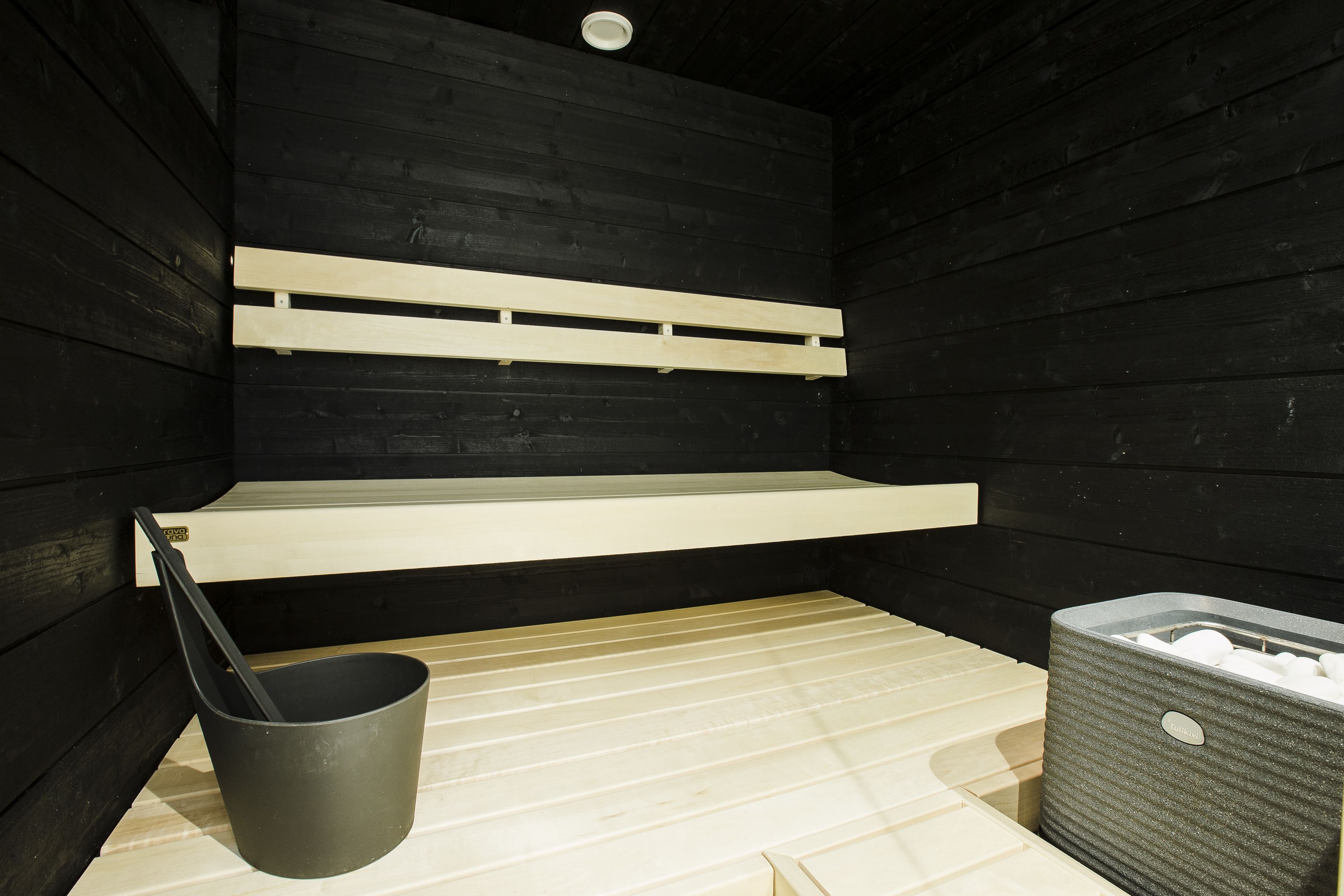 Una sauna con bancos de madera, un cubo y un contenedor de almacenamiento.