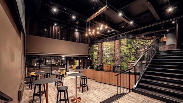 Un interior moderno con una zona de bar, asientos y una escalera que conduce a un nivel superior.