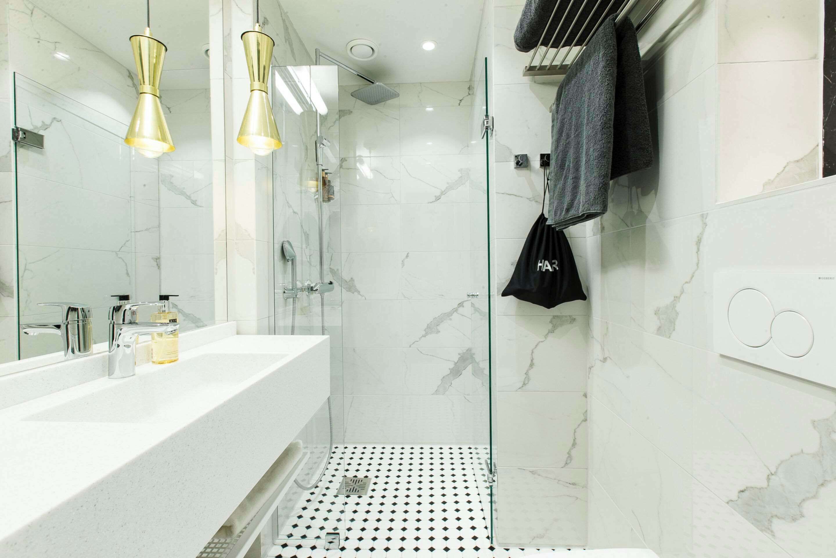 A modern bathroom with a glass-enclosed shower, a white marble sink, and two pendant lights.