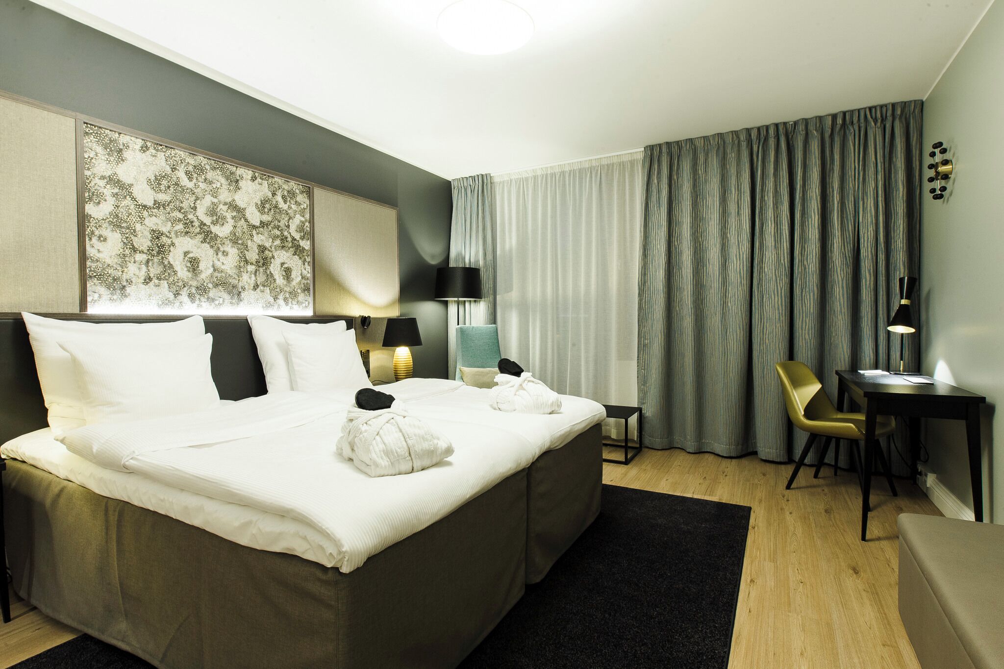 Una habitación de hotel con una cama grande, lámparas de noche, un escritorio y una silla.