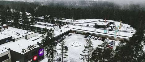 Un estacionamiento cubierto de nieve con varios coches, un edificio con el letrero BioRex y una zona boscosa al fondo.