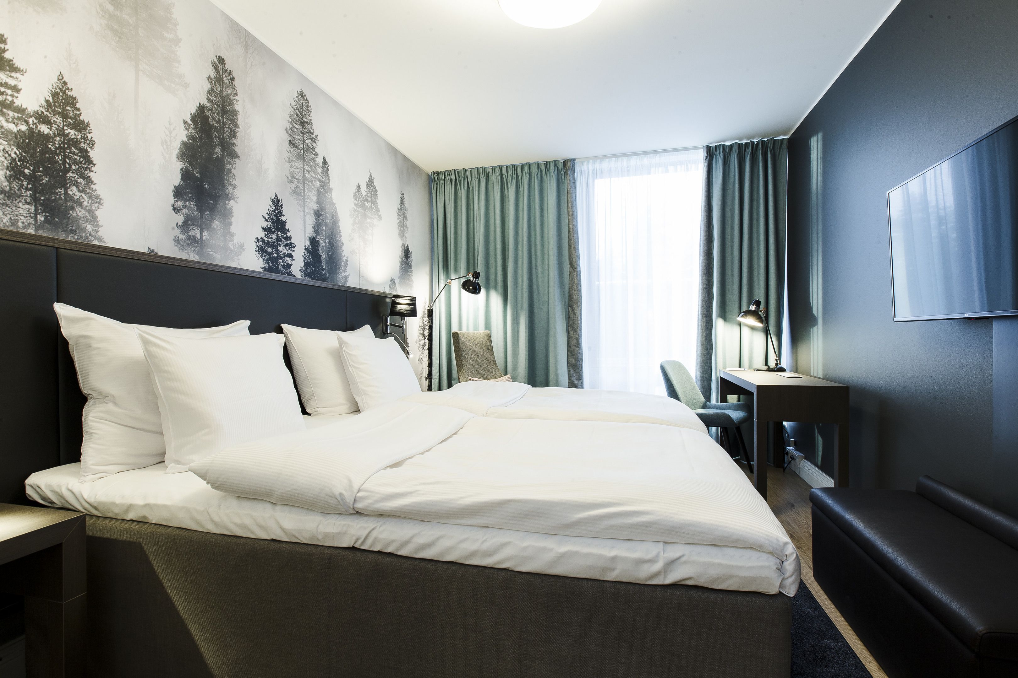 Habitación de hotel con una cama grande, un escritorio, una silla y un televisor.