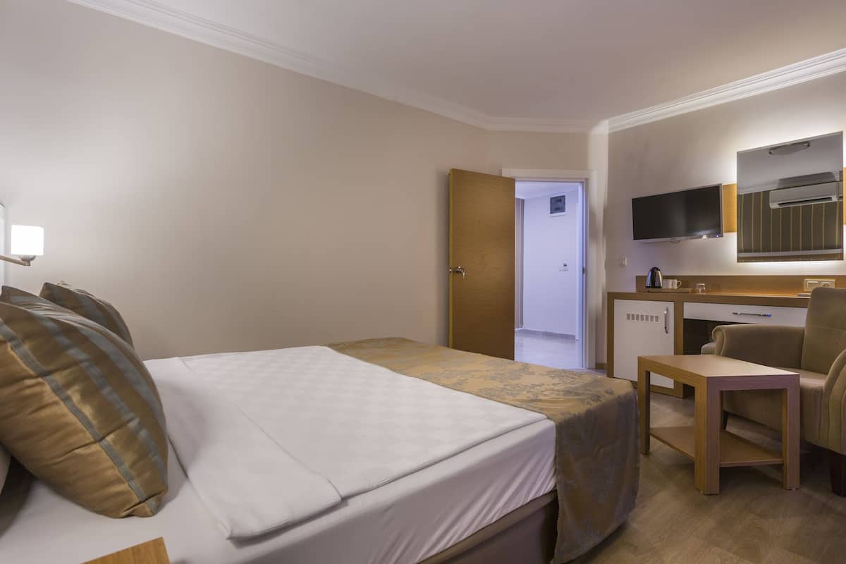 A hotel room with a bed, a desk, a chair, a TV, and a kitchenette.