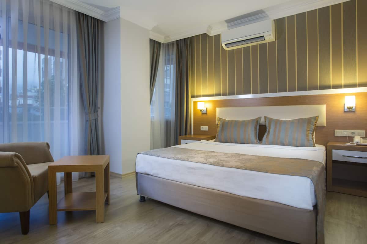 A hotel room with a large bed, a wooden nightstand, a desk, and a chair.