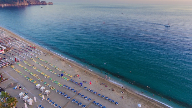 An aerial view of a beach with rows of sunbeds and umbrellas, a clear sky, and calm sea. - Lonicera City Hotel (Alanya)