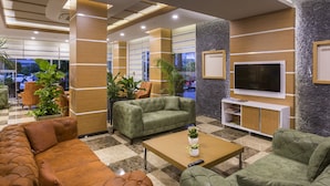 A modern lobby with leather sofas, a coffee table, and a TV on a stone wall. - Lonicera City Hotel (Alanya)