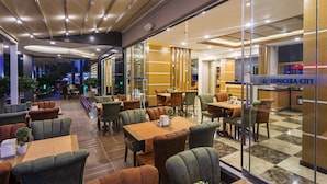 A modern restaurant with a checkered floor, green and brown upholstered chairs, and a sign reading "LONICERA CITY". - Lonicera City Hotel (Alanya)