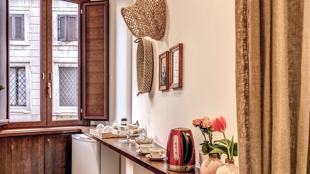 A kitchen with wooden cabinets, a white dishwasher, a red kettle, and a vase with flowers. - Approdo Ripetta (Rome)