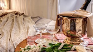 A table with a champagne bottle, two glasses, a decorative bowl, and some flowers on a patterned tablecloth. - Approdo Ripetta (Rome)