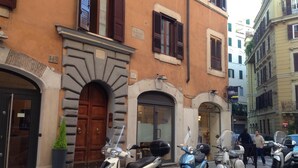 A row of parked scooters in front of a building with a large wooden door and a small potted plant beside it. - Approdo Ripetta (Rome)