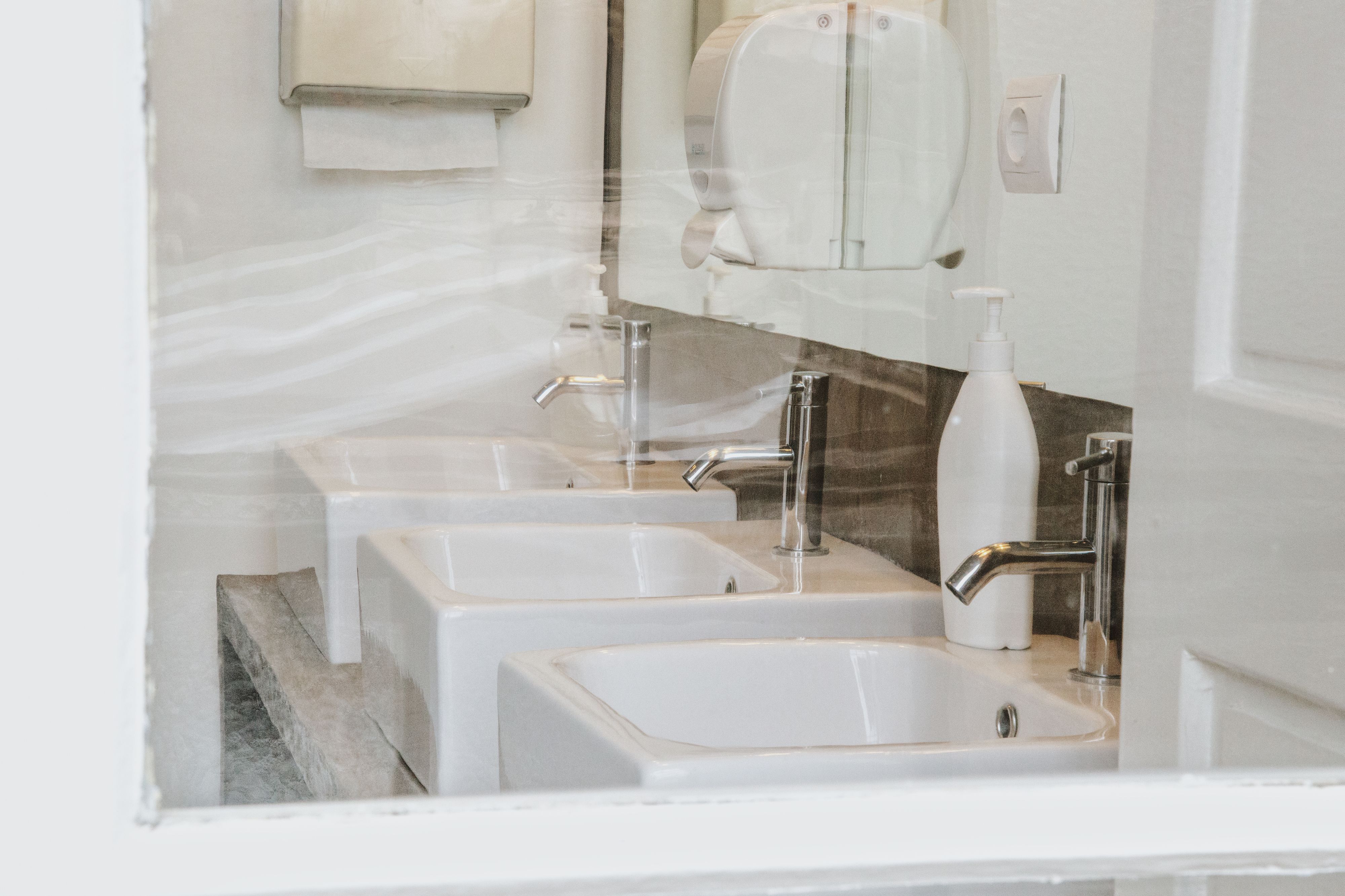 A bathroom with three sinks, a mirror, and a soap dispenser.