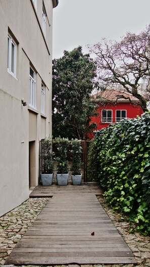 A narrow wooden pathway leading to a building with a red facade, surrounded by greenery and a fence. - Porto Spot Hostel (Porto)