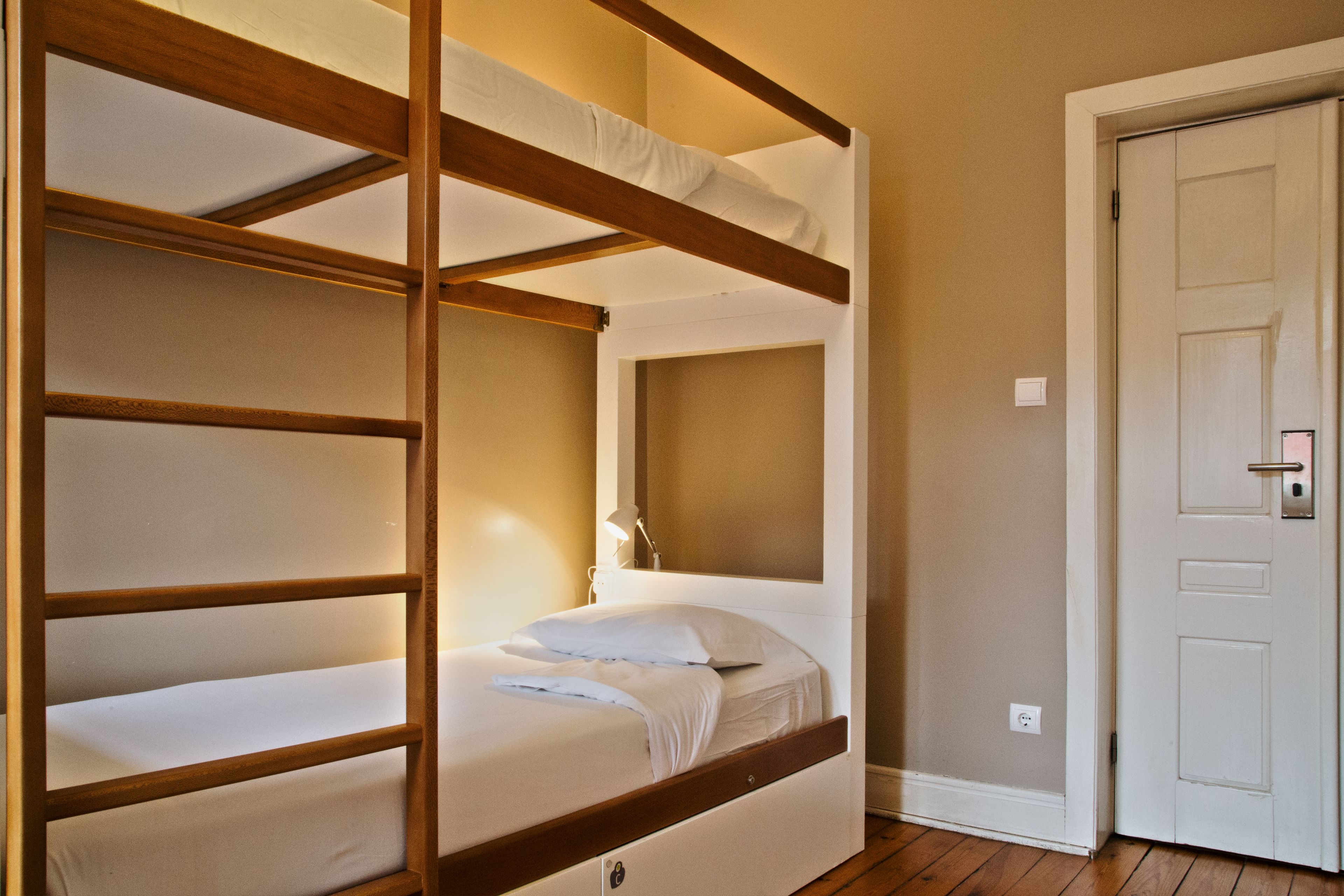 A bunk bed room with a wooden frame, a bedside table with a lamp, and a door.