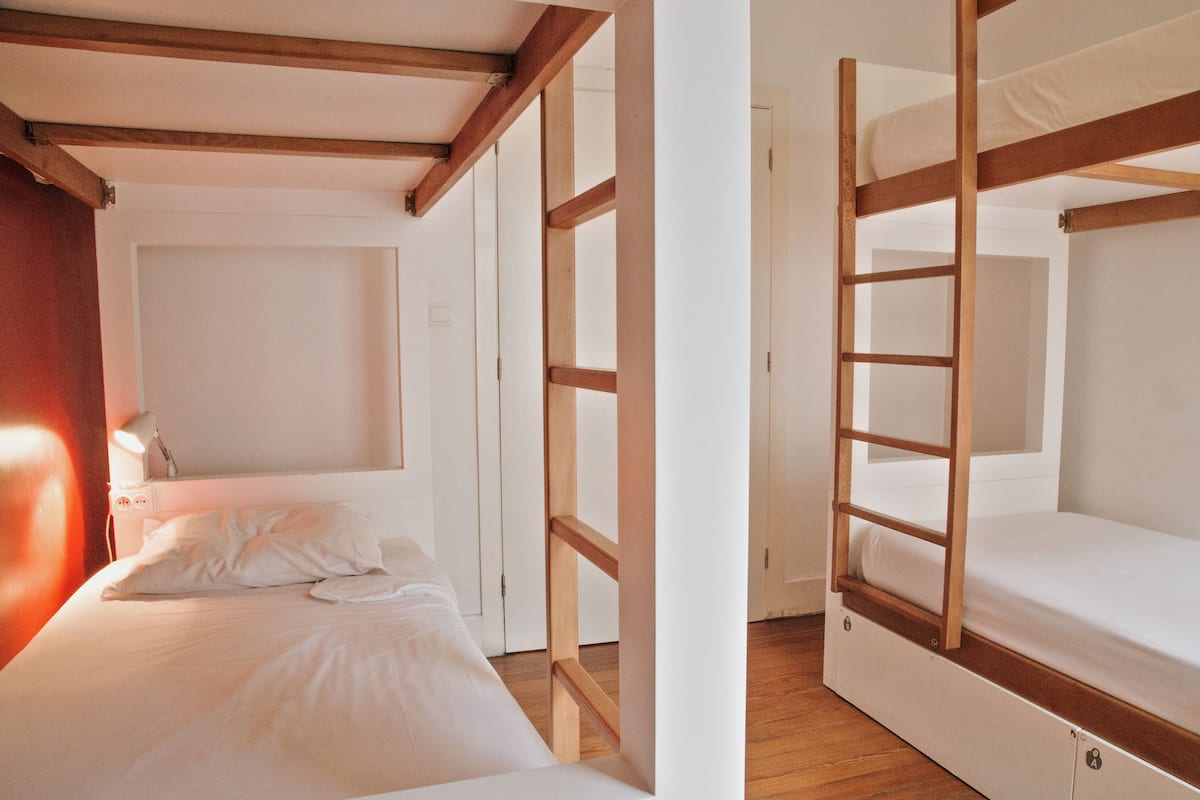 A bunk bed room with a wooden ladder, a bedside table, and a white wall.