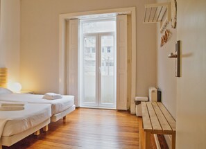 Quarto de hotel com duas camas, um banco, uma mesa de cabeceira com abajur e uma porta de vidro corrediça que dá para uma área externa.