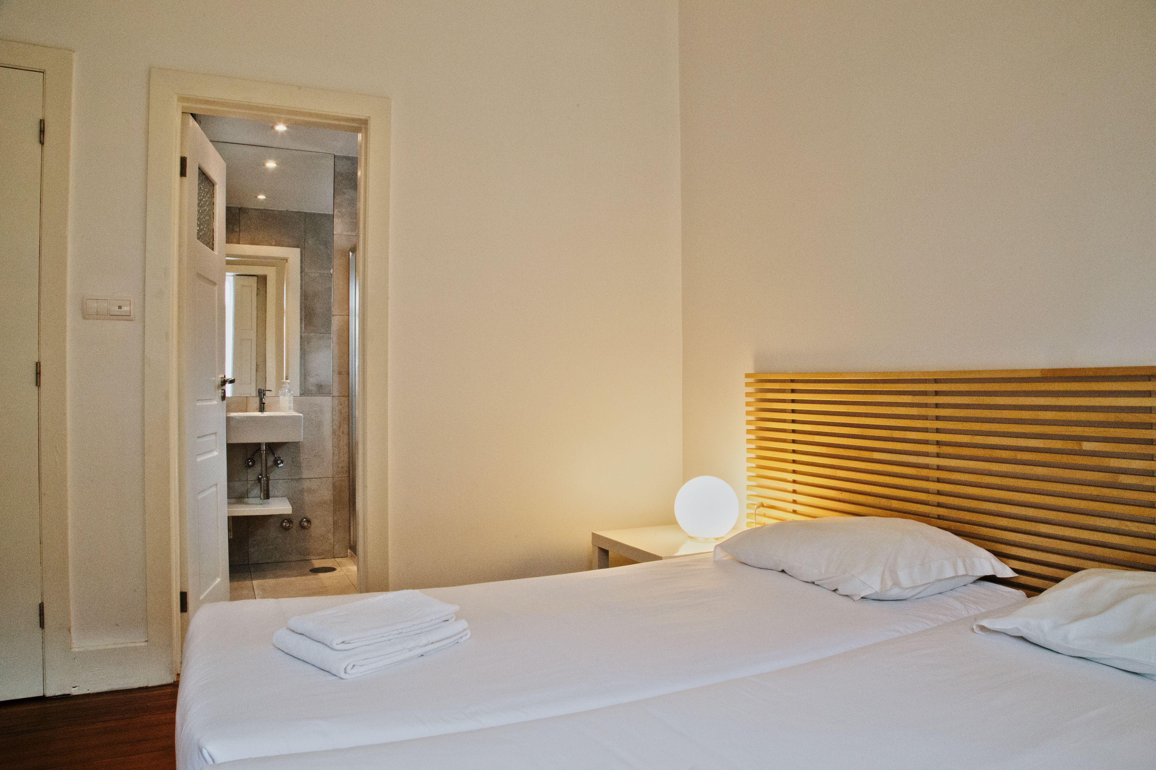 A hotel room with a bed, a bedside table with a lamp, and a bathroom visible through an open door.