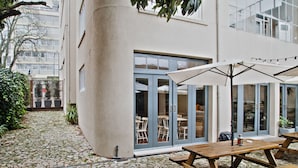 A courtyard with stone flooring, wooden picnic tables, and umbrellas.