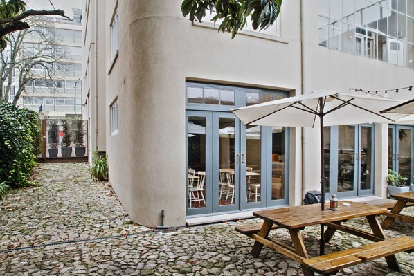 A courtyard with stone flooring, wooden picnic tables, and umbrellas. - Porto Spot Hostel (Porto)