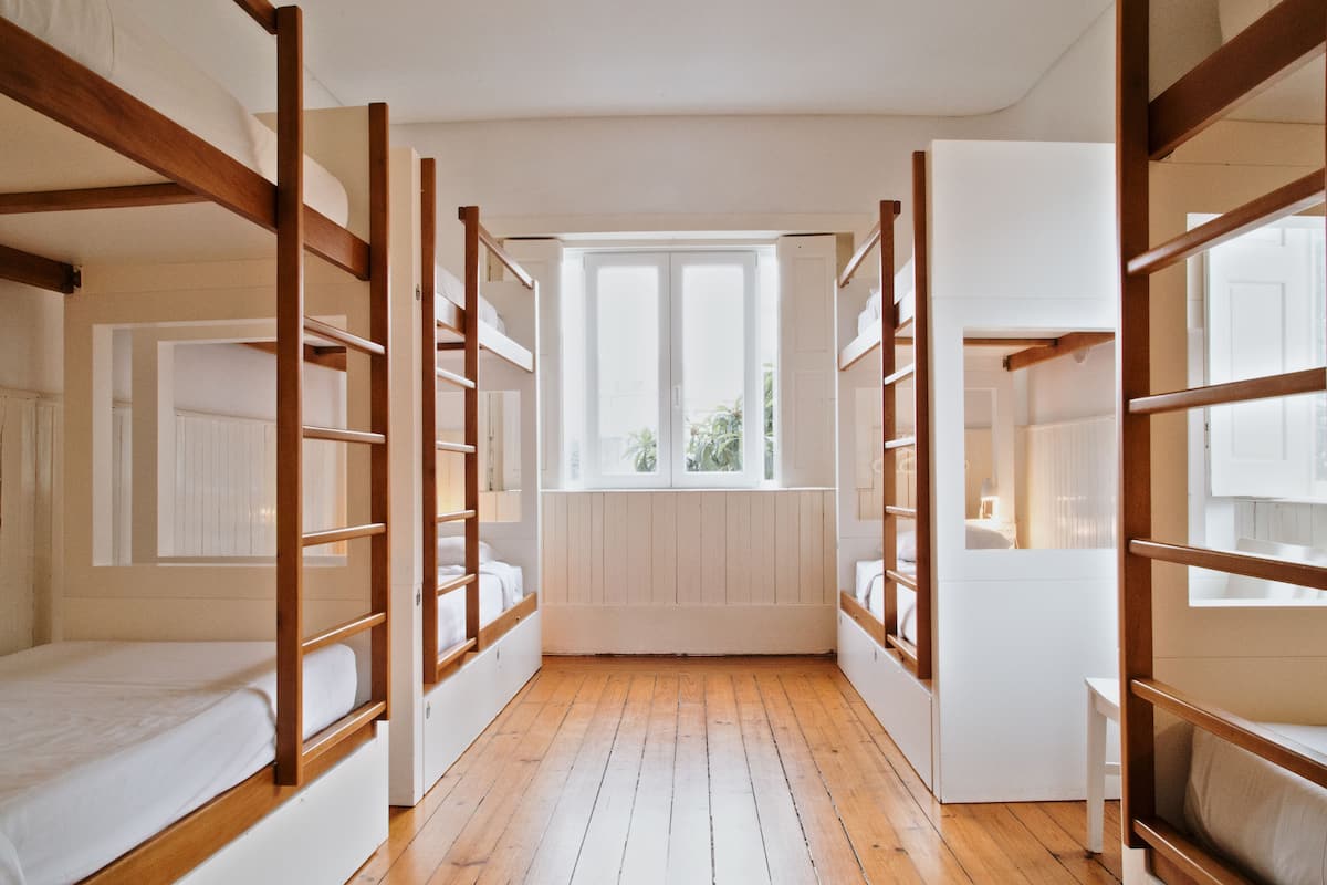 A dormitory room with bunk beds, a window, and wooden flooring.