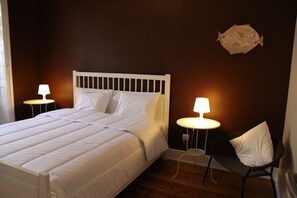 A neatly made bed with white bedding, two bedside tables with lamps, a dark wooden floor, and a wall-mounted fish decoration. - Porto Spot Hostel (Porto)