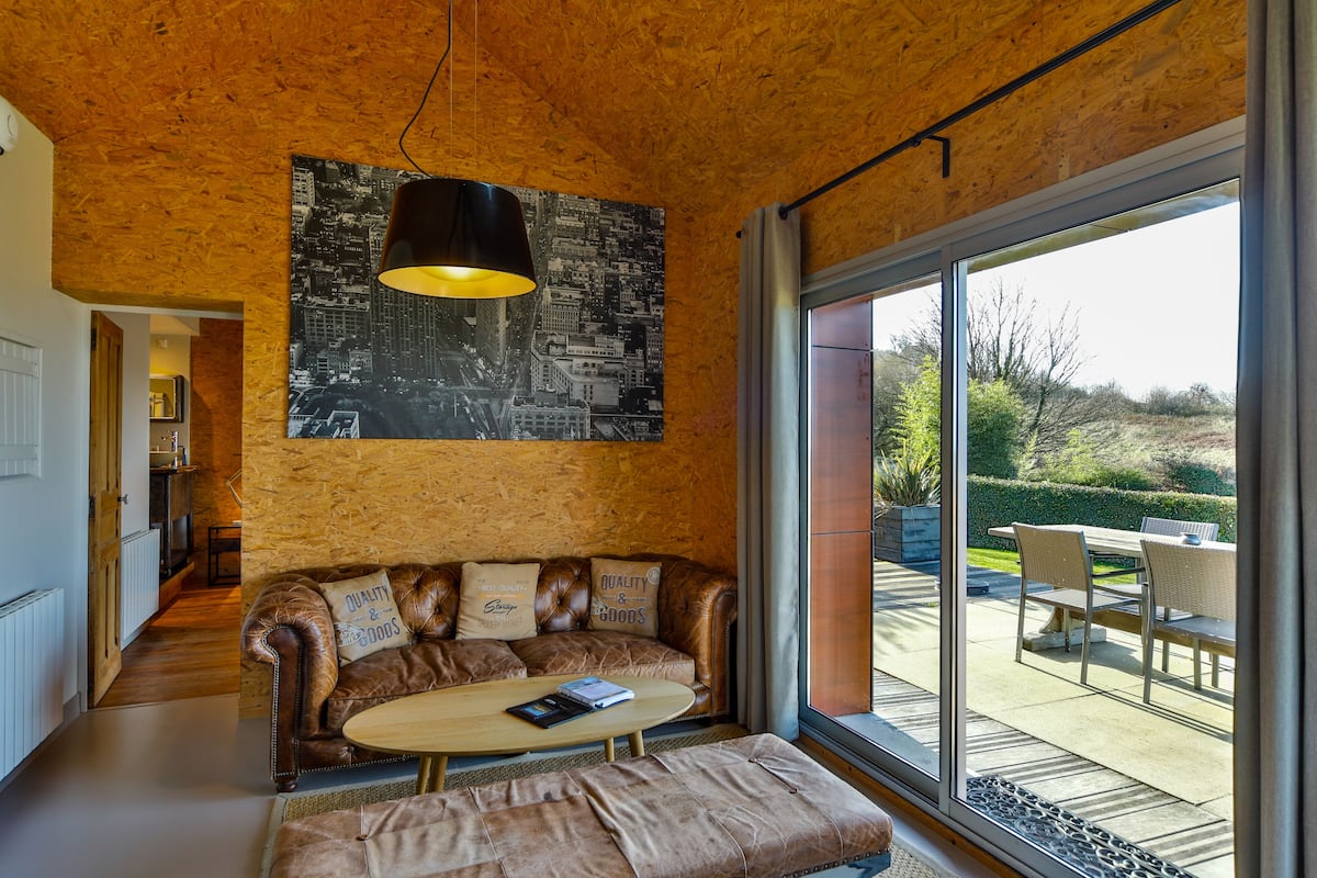 A modern living room with a leather sofa, a wooden coffee table, and a large window offering a view of the outdoors.