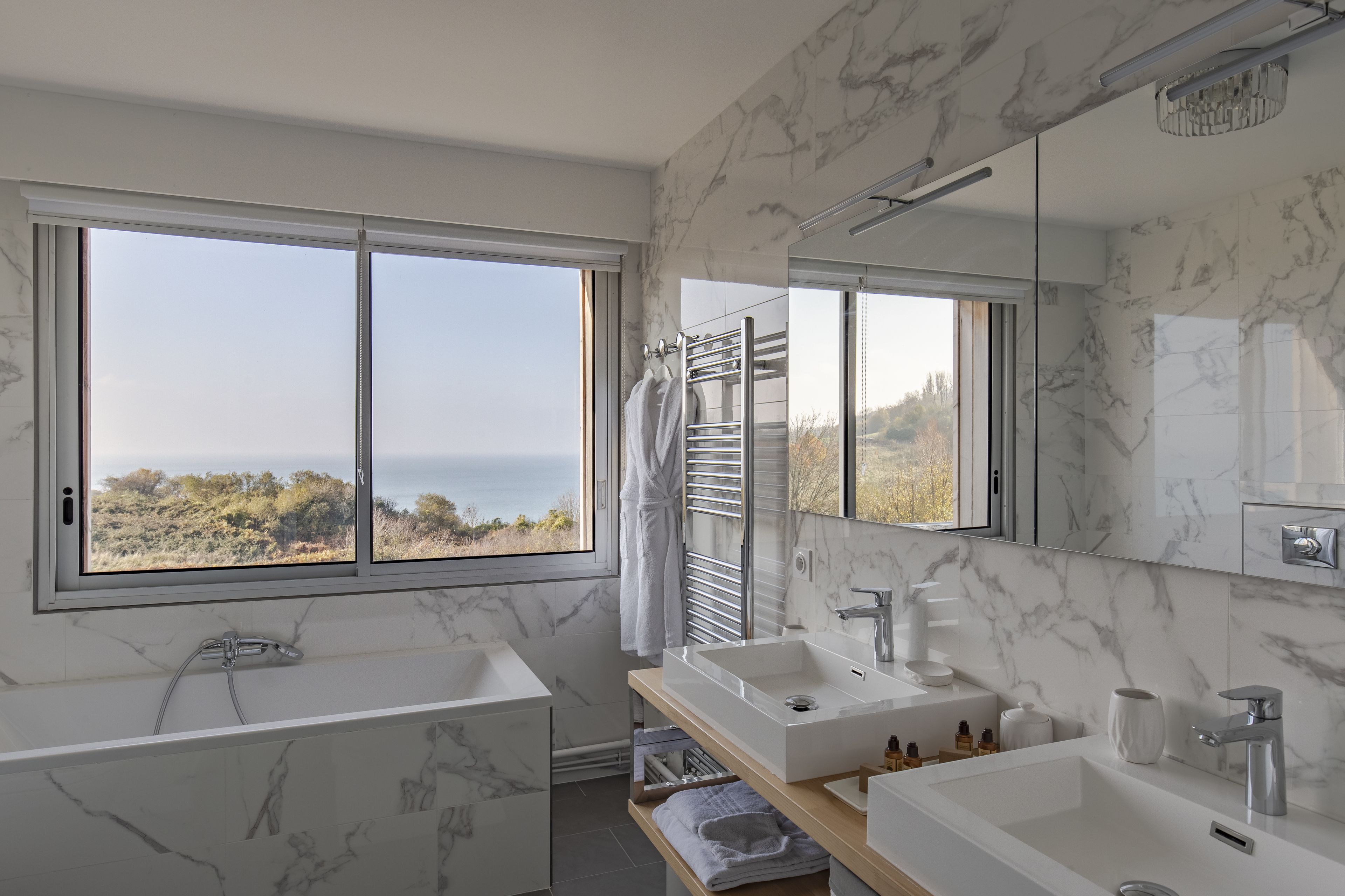 Un bagno moderno con una grande finestra, due lavabi, una vasca e uno schienale in marmo.