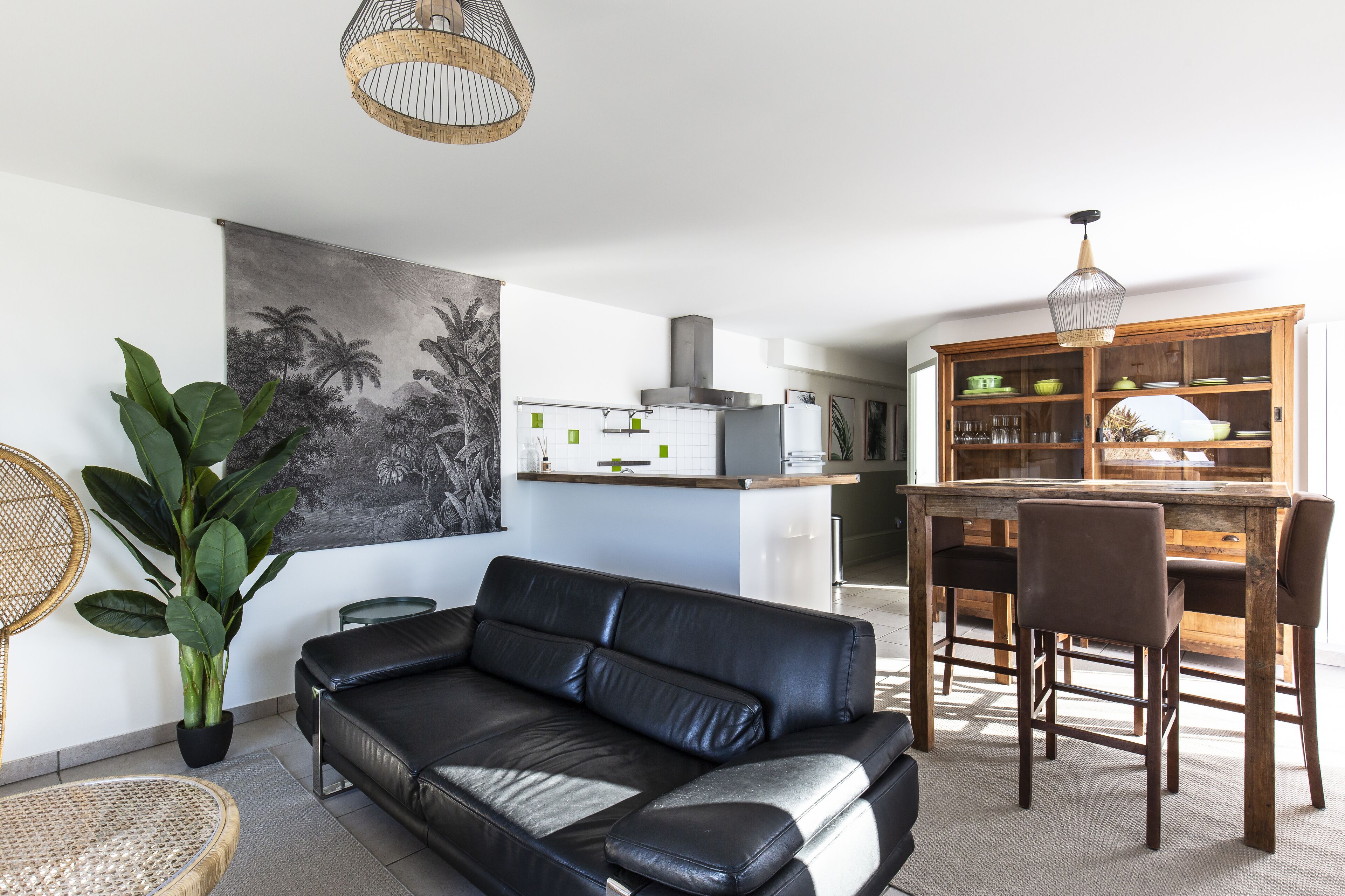 Una sala de estar moderna con un sofá de cuero negro, una mesa de comedor con sillas, una zona de cocina y un mueble grande de madera.