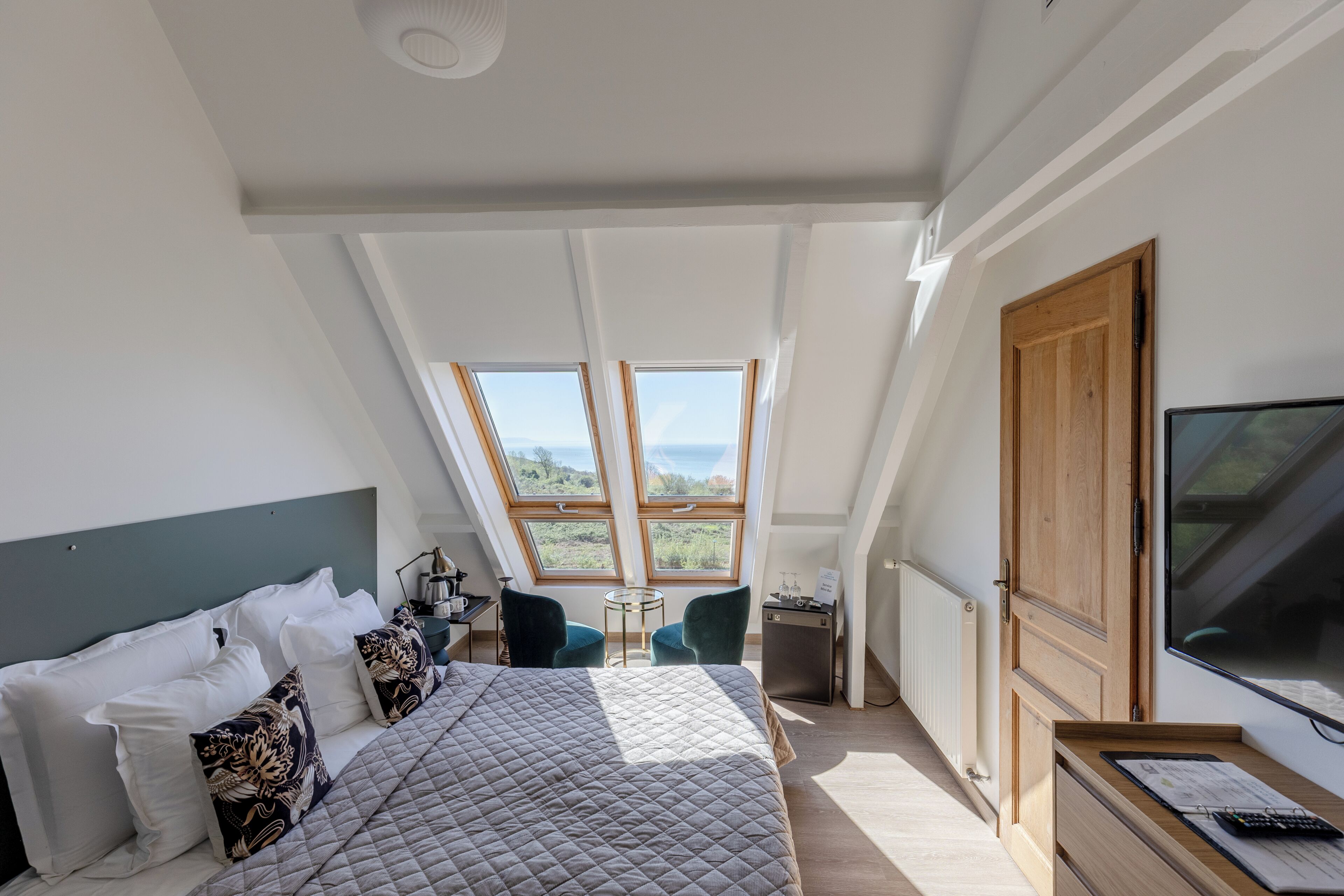 A bedroom with a large bed, a desk, a TV, and a view through the skylight.