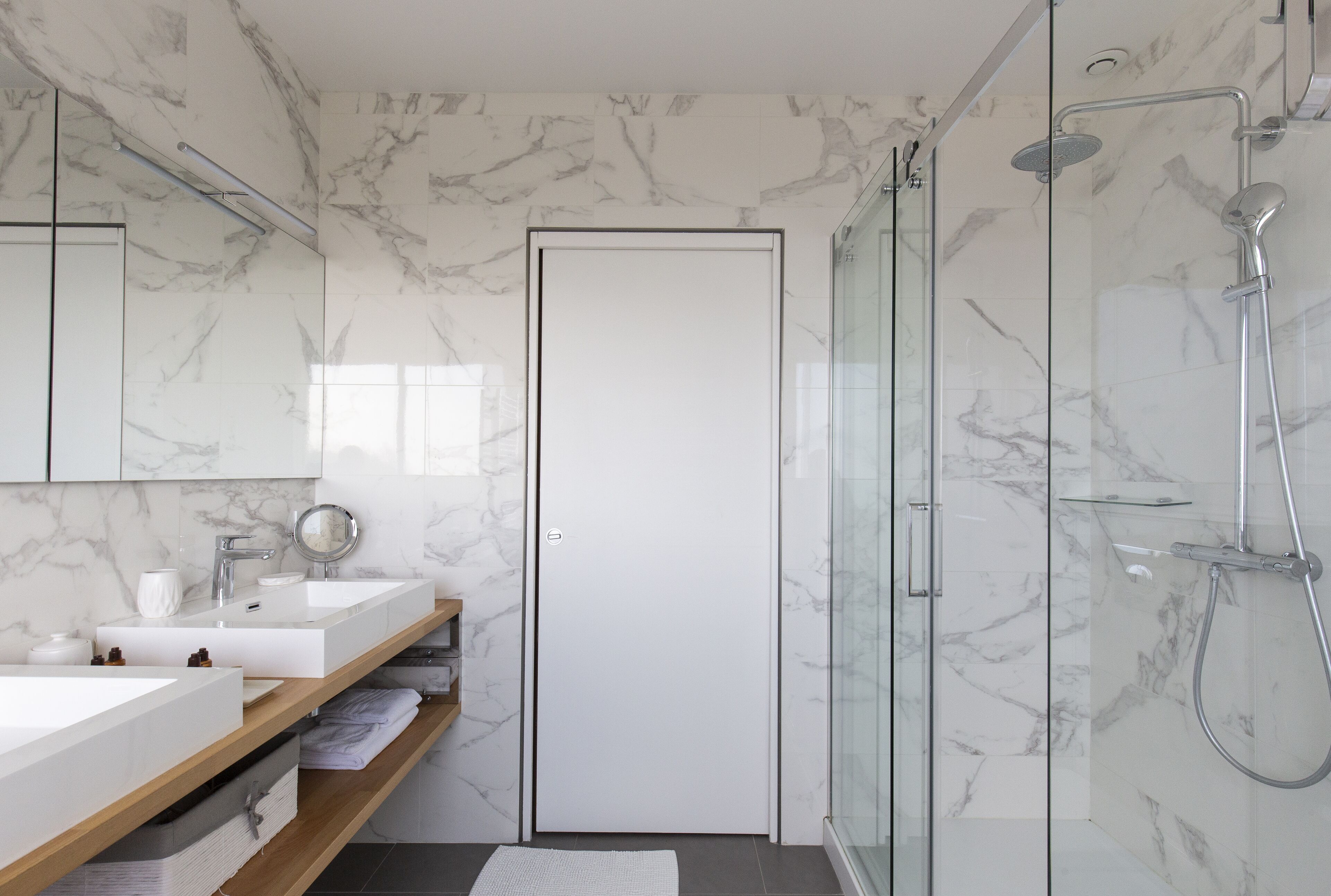Une salle de bain moderne avec des murs en marbre, une douche en verre et une porte blanche.