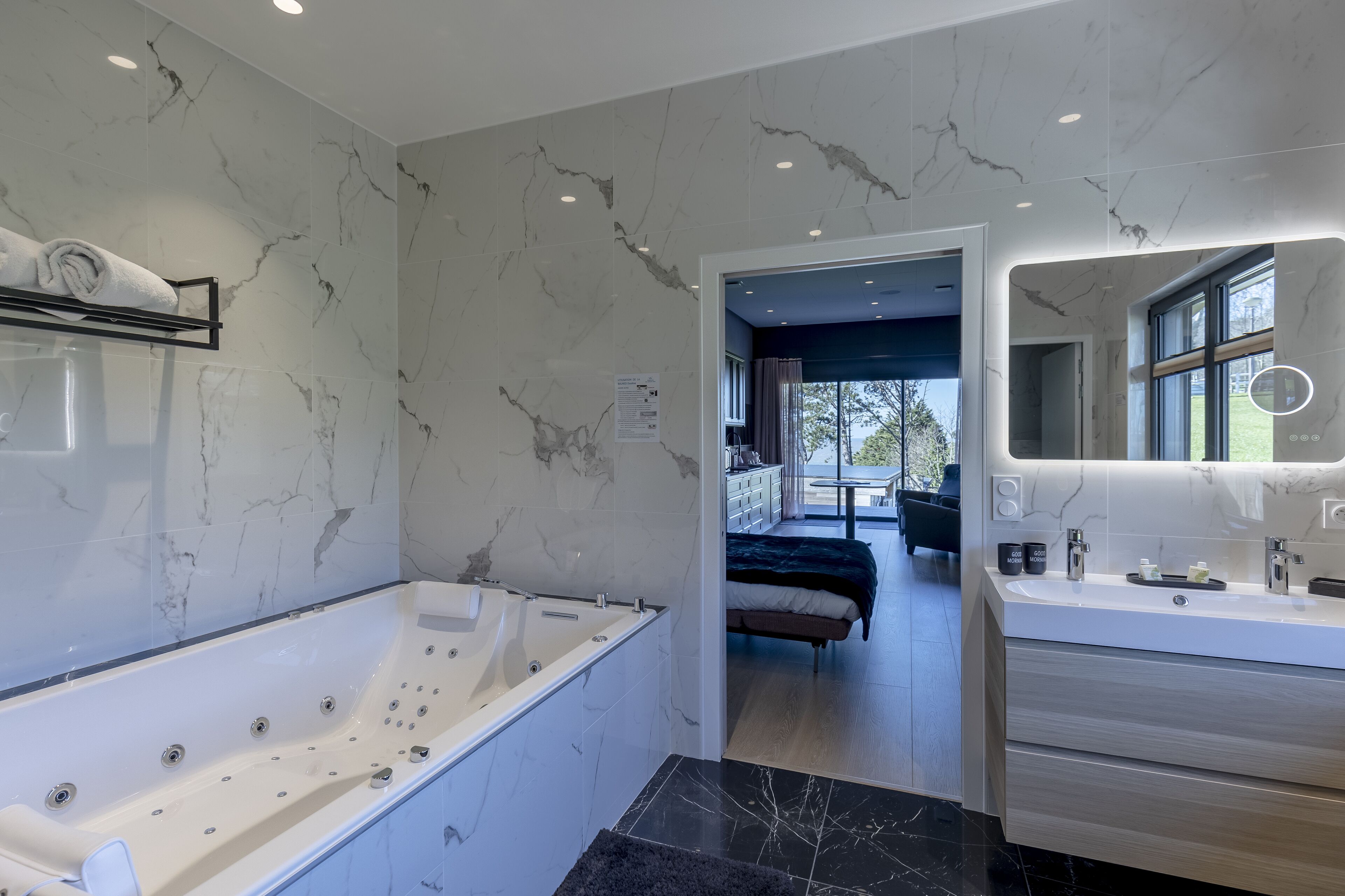 A modern bathroom with a large bathtub, a vanity with a mirror, and marble walls.