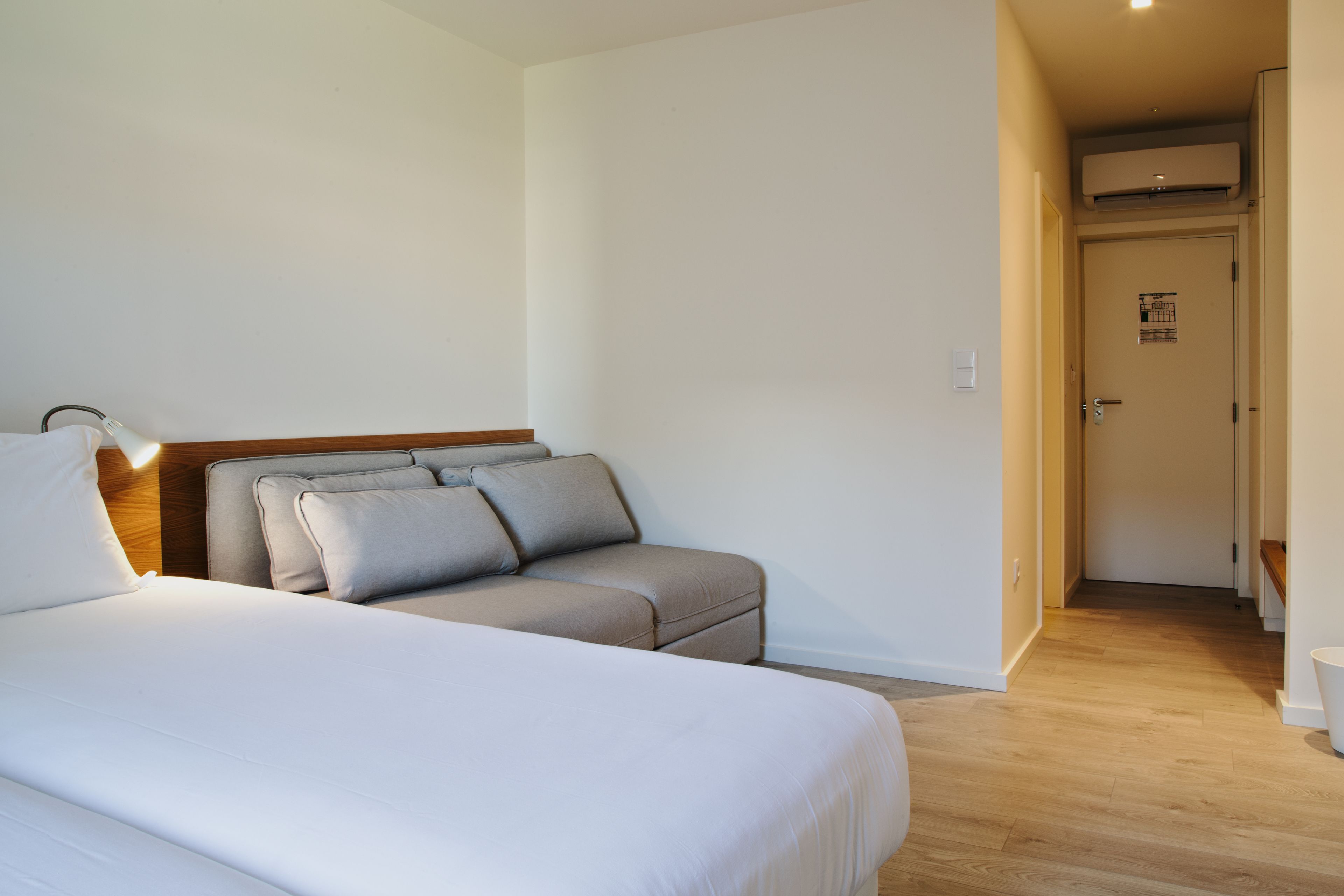 A hotel room with a bed, a sofa, a bedside table, and a door leading to another room.