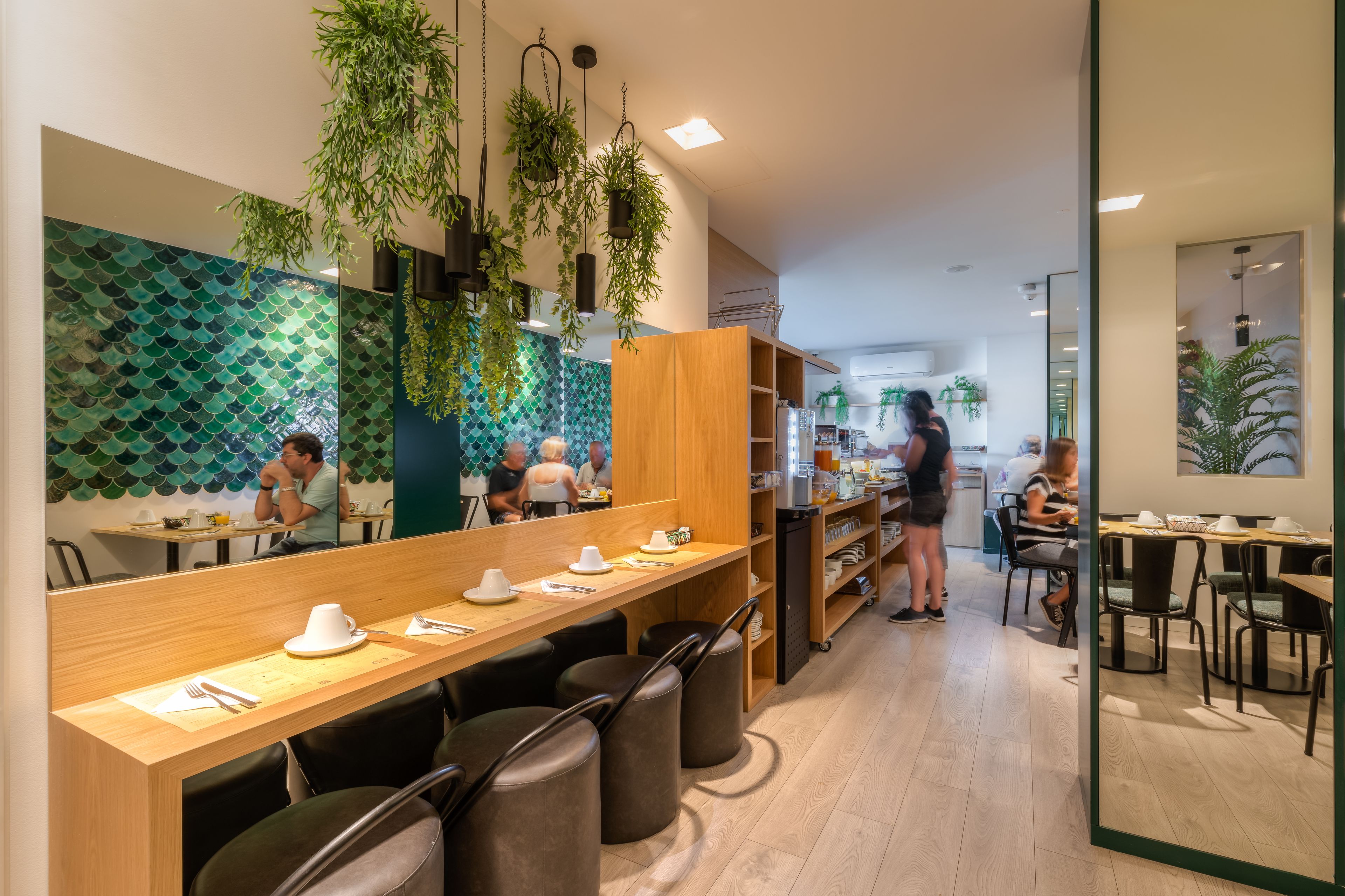 Un restaurante moderno con mesas de madera, taburetes negros y plantas colgantes.