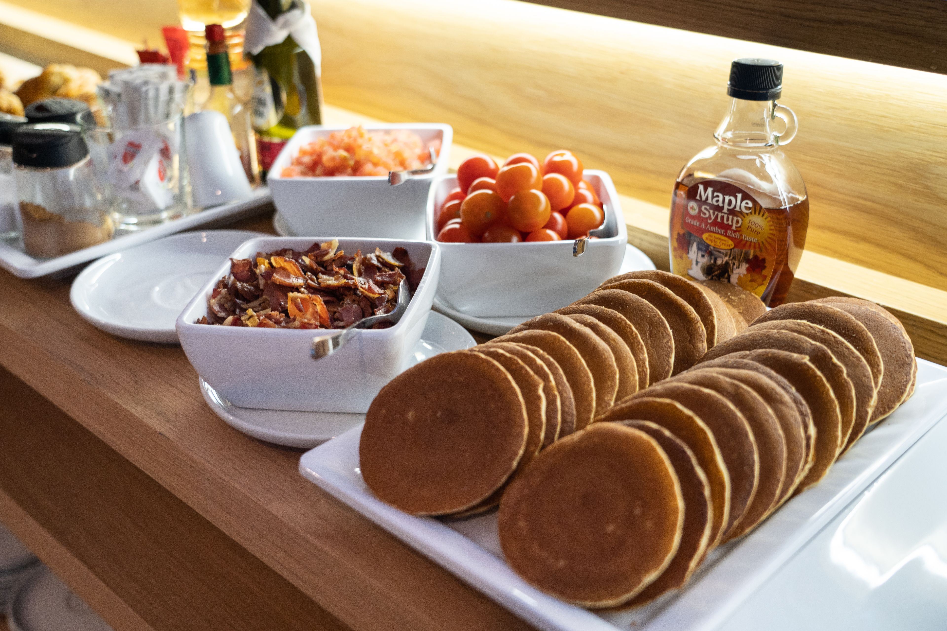 A breakfast buffet with pancakes, tomatoes, and maple syrup.