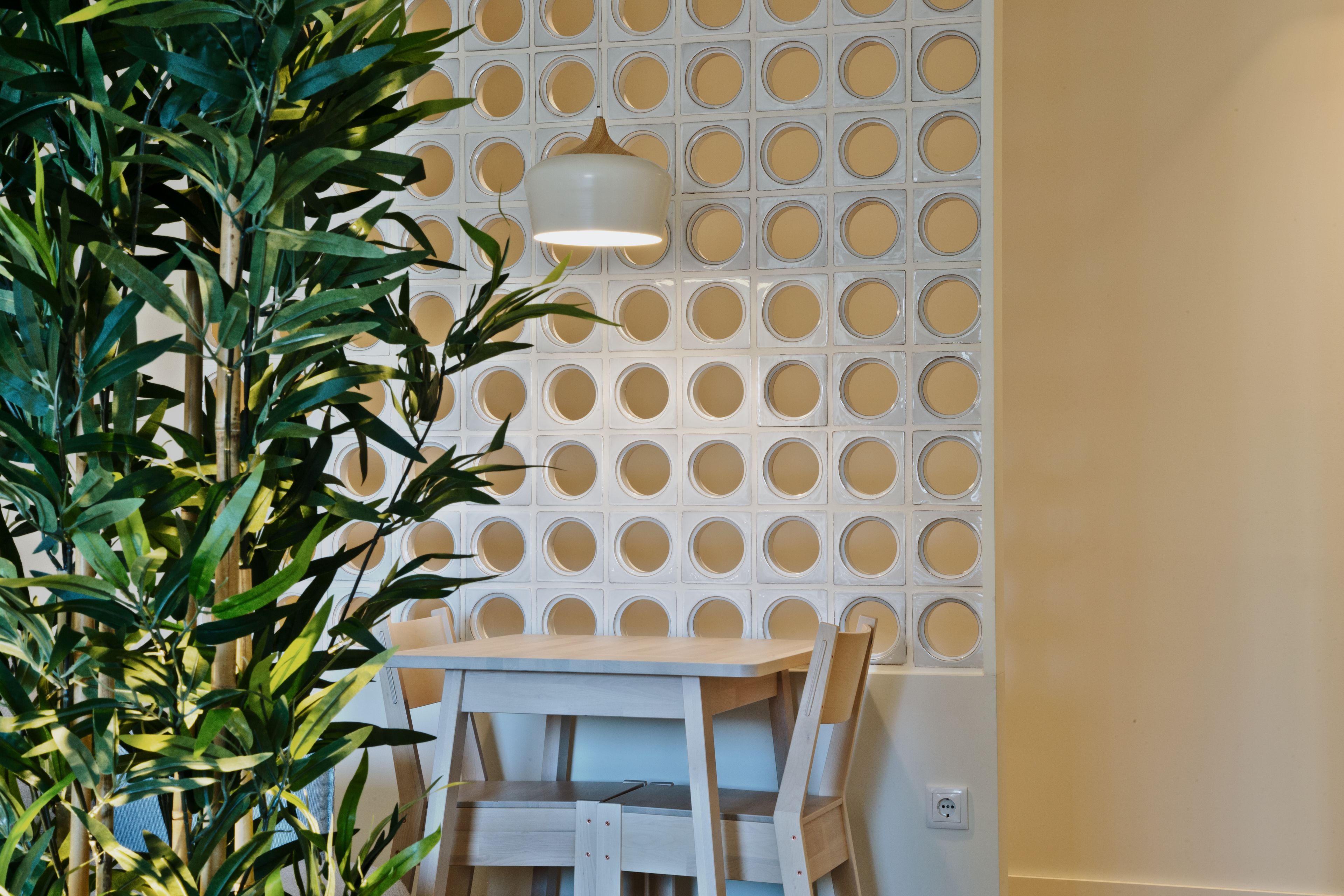 A dining area with a white table and chairs, a wall with circular cutouts, and a hanging light fixture.