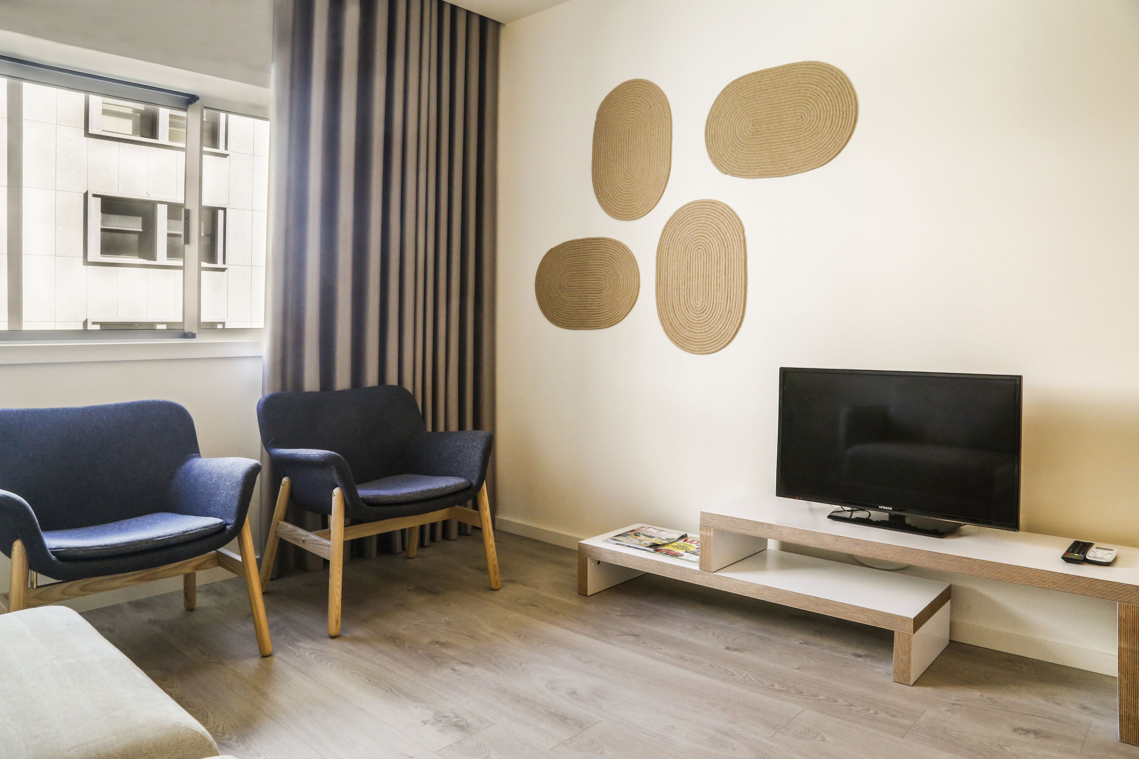 Una sala de estar moderna con dos sillones azules, un televisor sobre un mueble de madera y una revista en un estante.