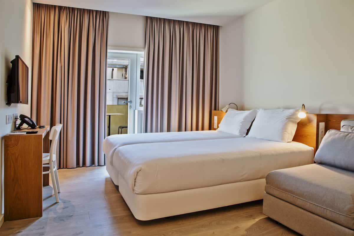 A hotel room with a bed, a desk, a chair, and a television.
