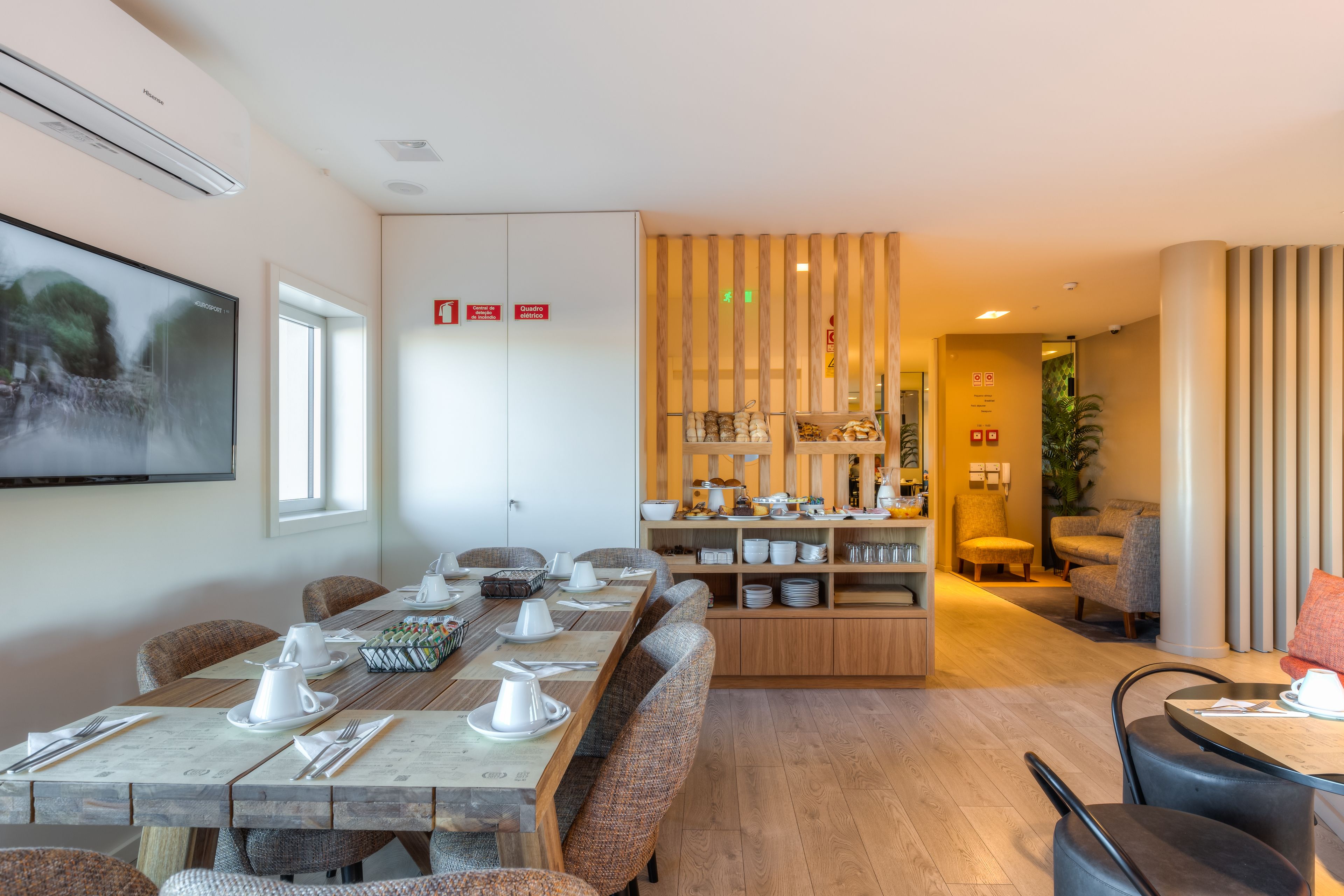 Un espace repas moderne avec une longue table en bois dressée pour un repas, un coin cuisine équipé de divers plats et ustensiles, et un coin salon avec des fauteuils confortables.
