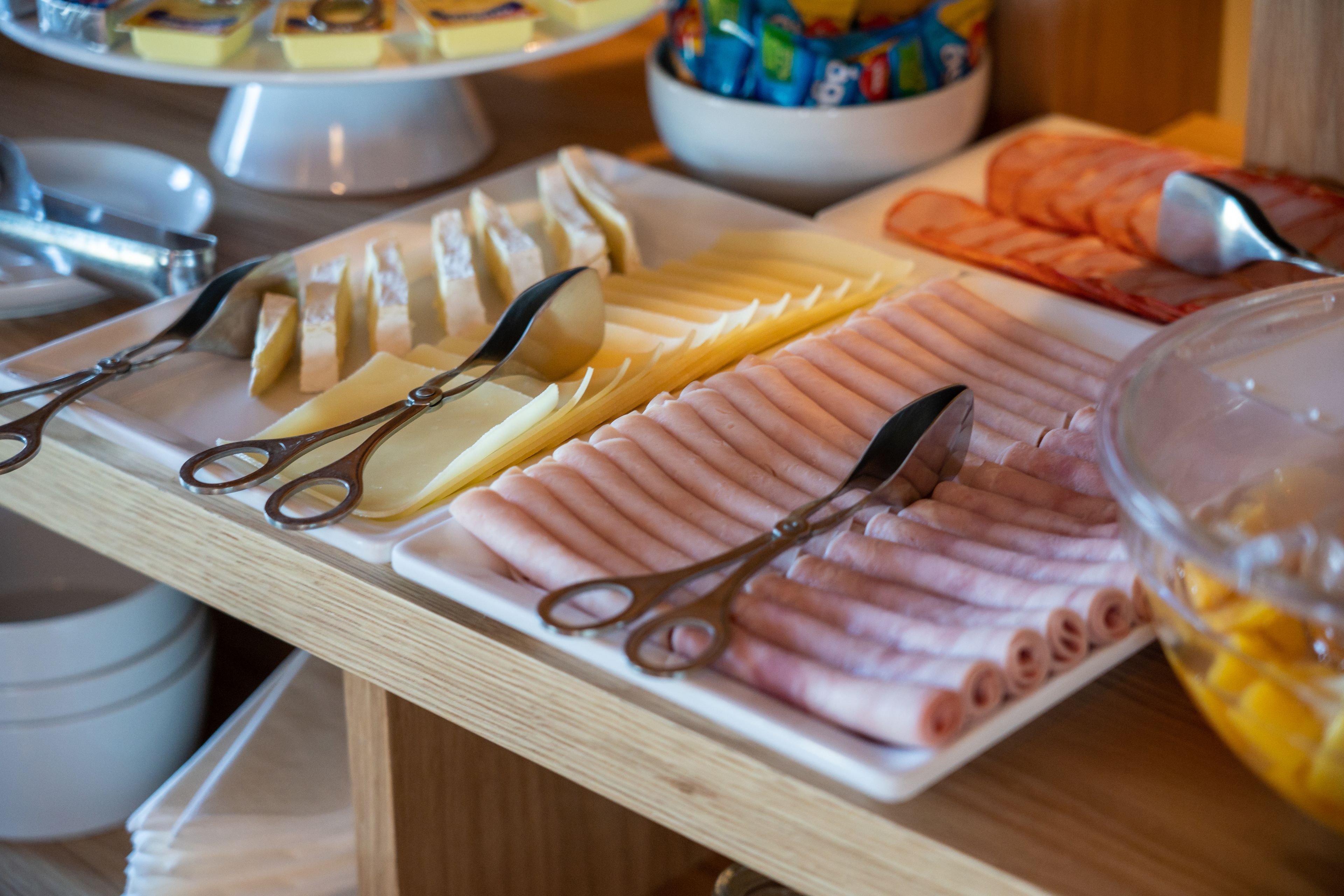 Una mesa de buffet con varios quesos, carnes y un bol de fruta.