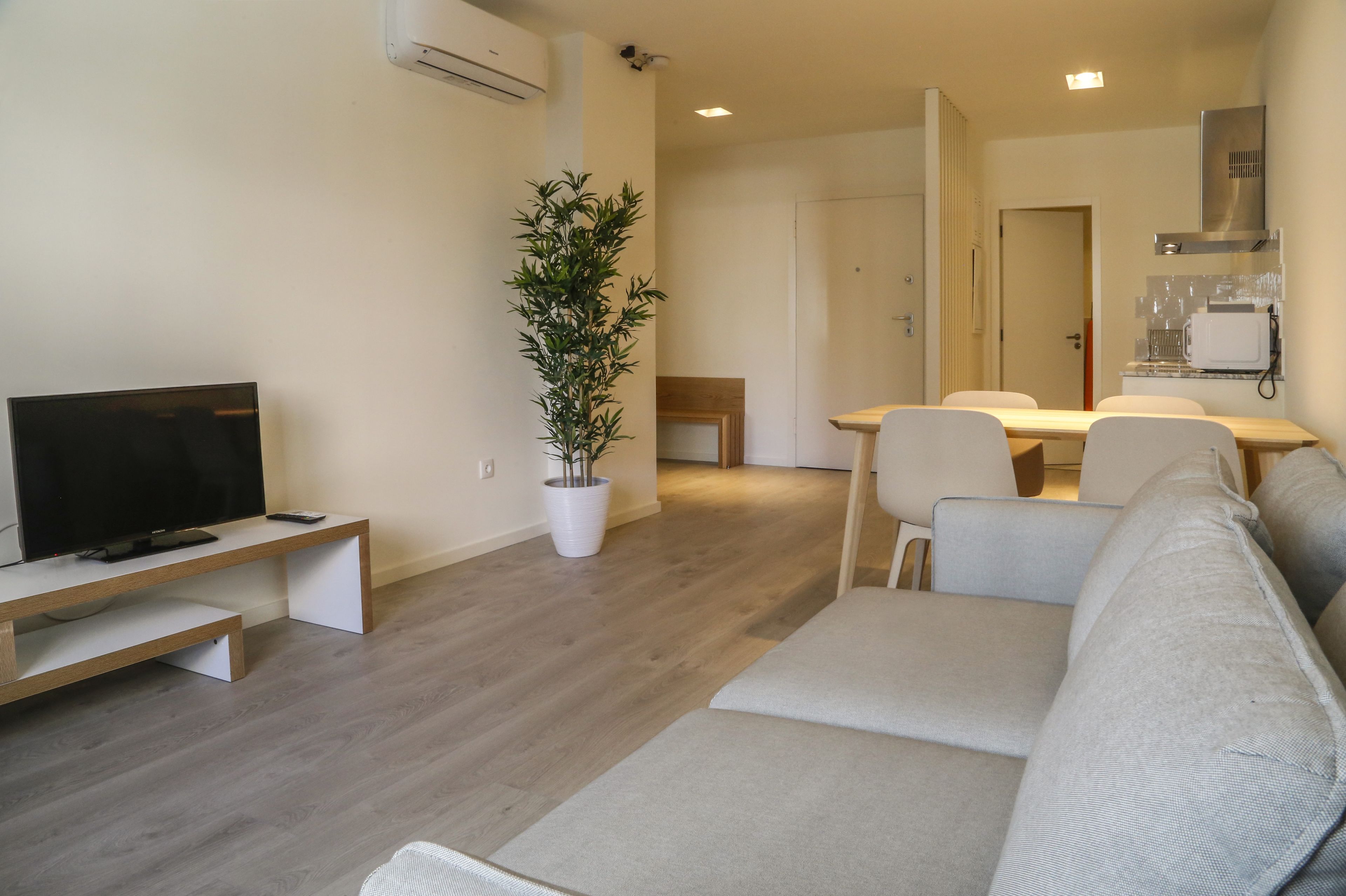 Una sala de estar moderna con un televisor de pantalla plana, un sofá, una mesa de comedor con sillas y una planta en maceta.