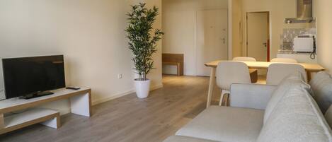 Una sala de estar moderna con un televisor de pantalla plana, un sofá, una mesa de comedor con sillas y una planta en maceta.