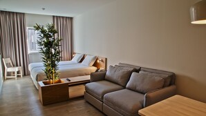 A modern hotel room with a bed, a sofa, a wooden nightstand, a bedside table, and a potted plant. - Hotel Spot Family Suites (Porto)